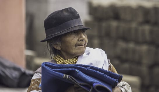 Eine alte Frau in traditioneller Kleidung mit Hut trägt eine blaue Decke