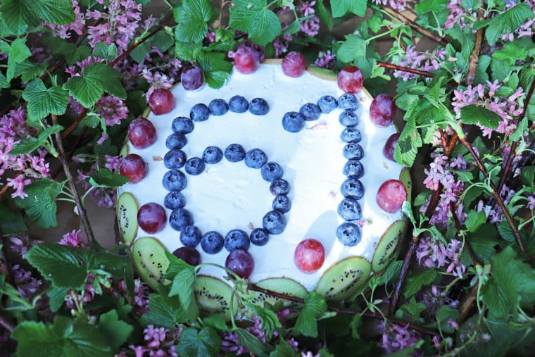 Eine mit lila Beeren verzierte Torte mit der Zahl 61, umrahmt von blühenden Zweigen