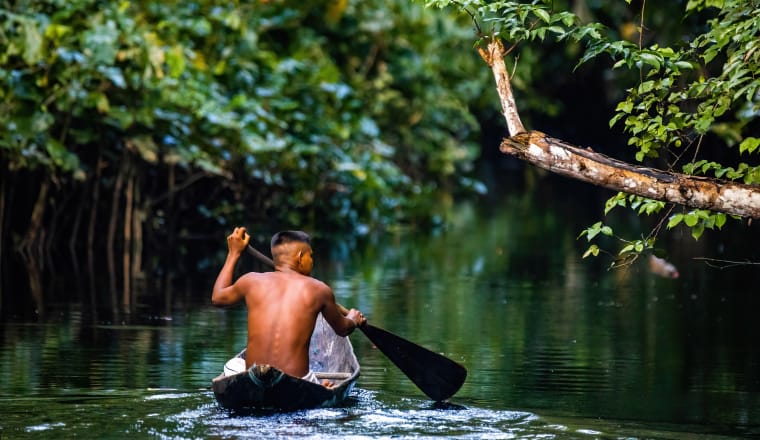 Mann vom Volk der Pirahã , der im Amazonas Regenwald in handgefertigtem Boot paddelt