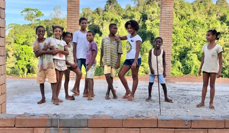 Neun brasilianische Kinder stehen in einem Rohbaum einer Schule. Im Hintergrund ist der Regenwald zu sehen.