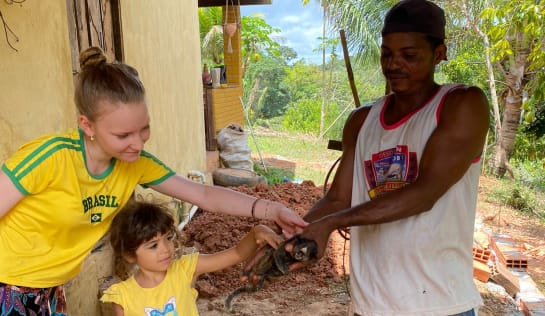 Der Ranger Rosenildo hat das verirrte Äffchen nach den Streicheleinheiten wieder in den Wald entlassen Junges Mädchen, Kind und Mann stehen unter einem Hausdach und streicheln einen kleinen Affen, den der Mann in der Hand hält