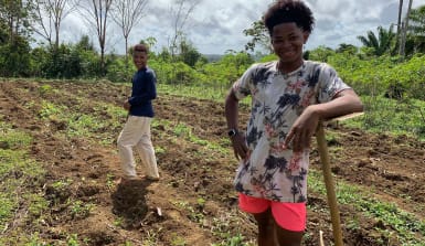 Kleine Pause bei der Feldarbeit: Daniel (links) und Carlos Zwei Jungs auf einem Feld, einer stützt sich auf einen Spaten, beide lachen