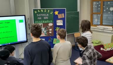 Schülerinnen und Schüler schauen auf ein Plakat mit den Worten Handys sammeln für den Regenwald.