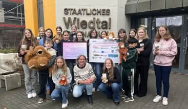 Schülerinnen und Schüler stehen vor einem Schulgebäude. Sie halten Sponsorenplakate und Stoffgorillas in die Höhe.