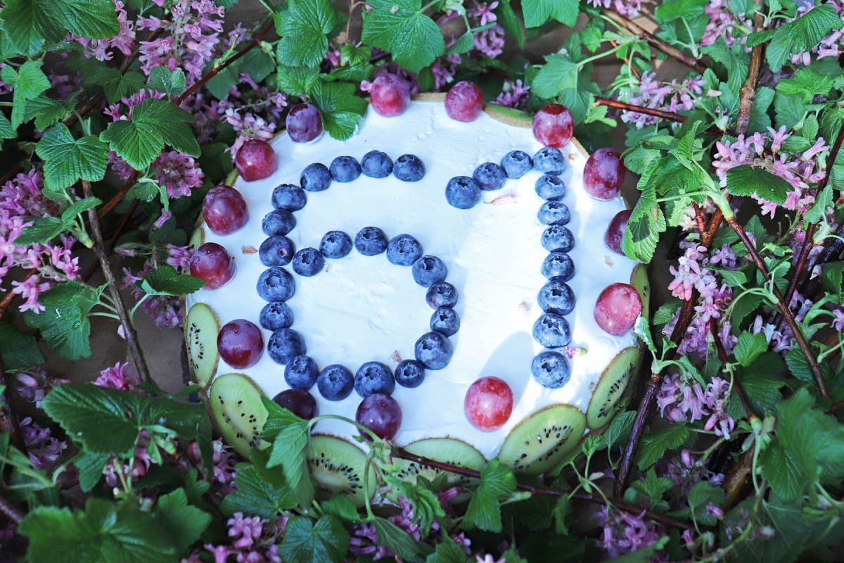 Bellas Geburtstagstorte Eine mit lila Beeren verzierte Torte mit der Zahl 61, umrahmt von blühenden Zweigen