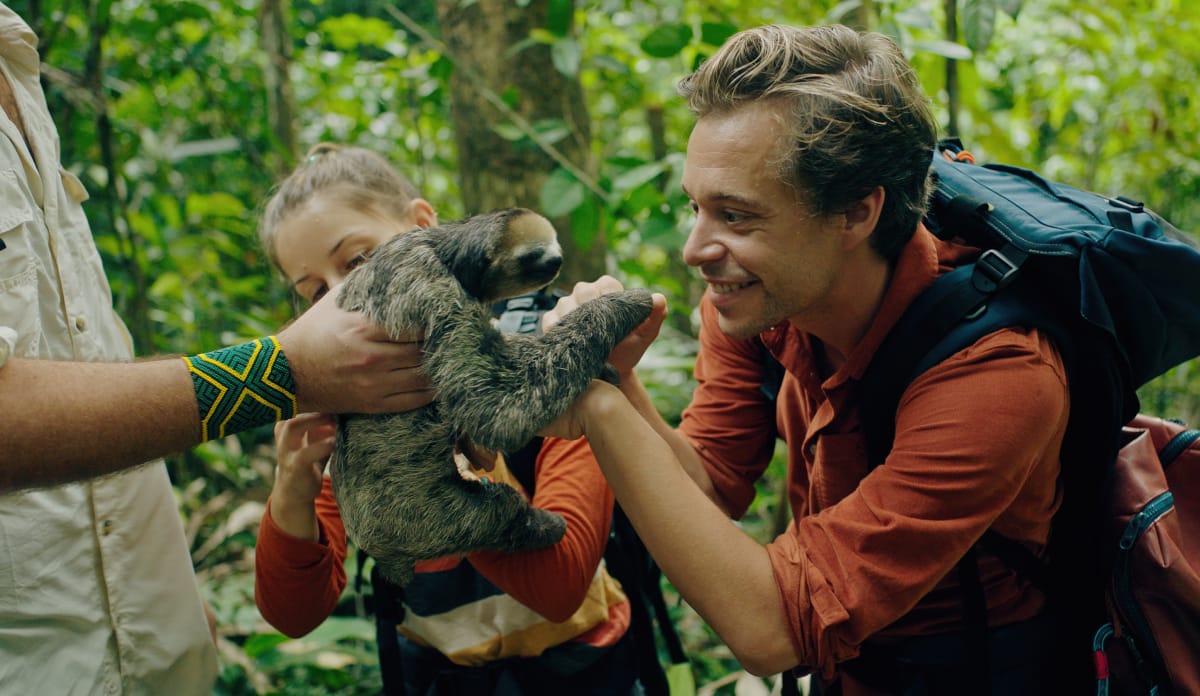 Natürlich trifft Tobi in Brasilien auch ein Faultier... Tobi und Marina berühren ein kleines Faultier, das von einem Mann gehalten wird, der Mann ist nur zum Teil zu sehen