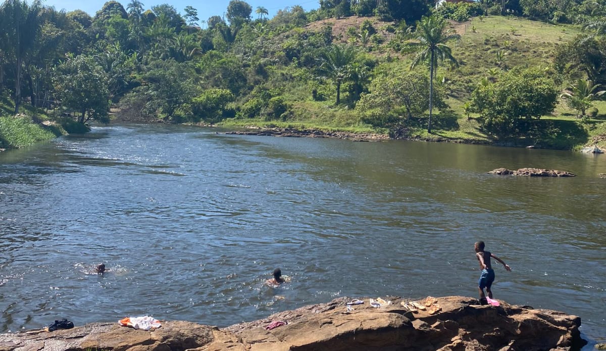 Flusslandschaft mit badenden Kindern, im Vordergrund flache Felsen, im Hintergrund Wald und Wiesen