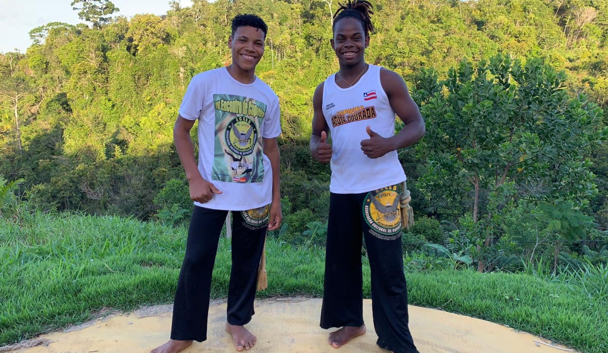 Daniel und Caíque freuen sich auf euch! 2 Jungen im weißen Shirt und schwarzer Hose vor Regenwaldkulisse