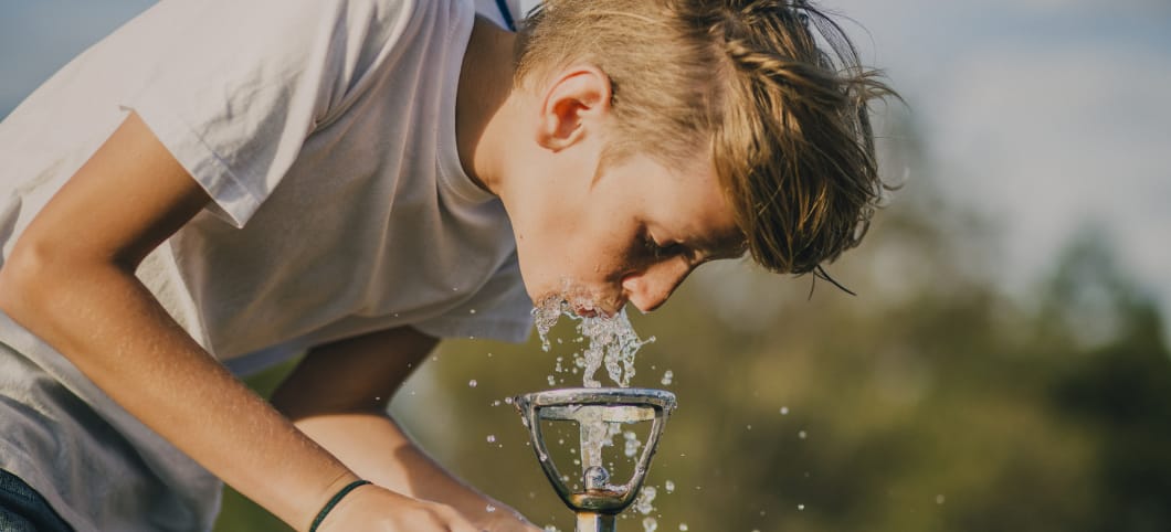 Ein Jugendlicher trinkt Wasser aus einem Wasserhahn in der Natur