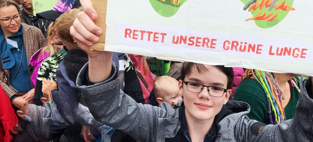 ein Teenager hält ein Regenwaldschutz-Plakat in die Kamera mit der Aufschrift Rettet unsere grüne Lunge