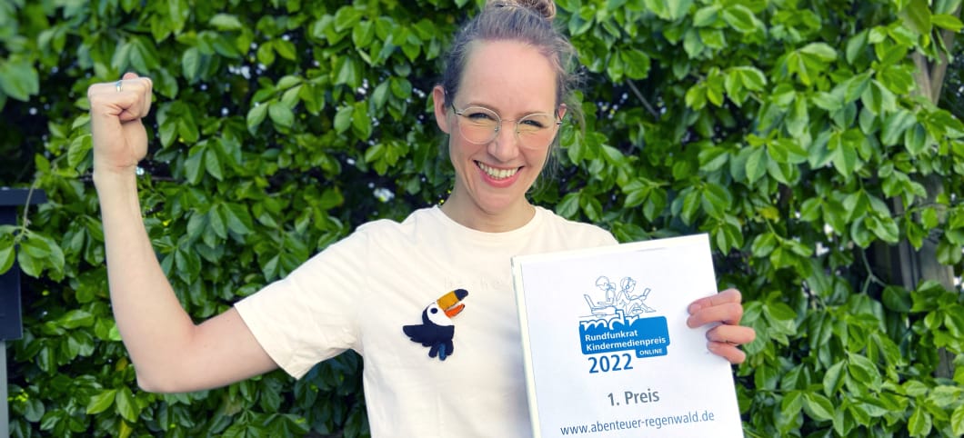 Kathrin von Abenteuer Regenwald hält lachend die Urkunde des MDR Kinder-Online-Preises in die Kamera