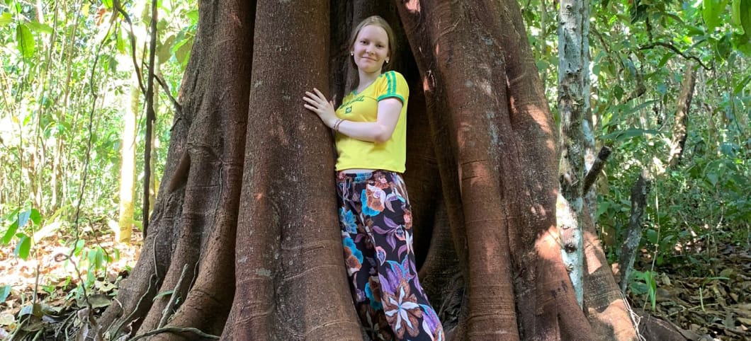 Annalena und ein Urwaldriese im Atlantischen Regenwald in Brasilien Eine junge Frau steht zwischen den großen Brettwurzlen eines Urwaldbaumes