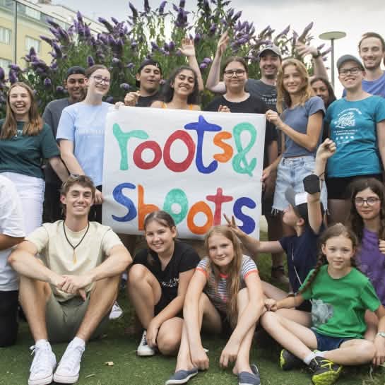 Eine Gruppe Jugendlicher hält ein Transparent mit der Aufschrift Roots & Shoots in den Händen